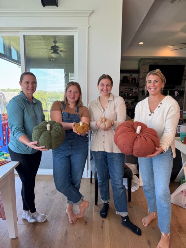 Four women holding pumpkins made out of sweaters