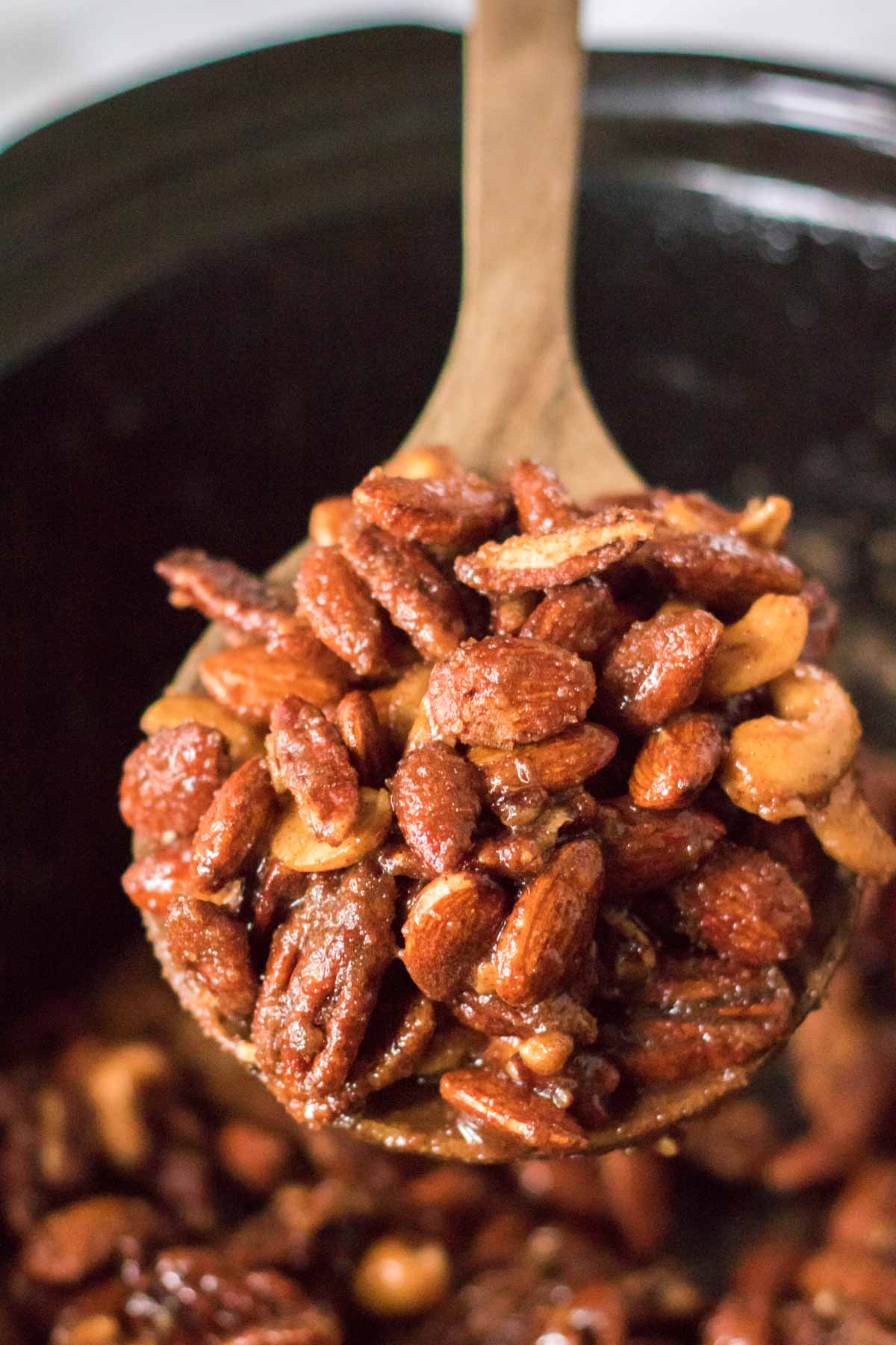 spoon full of candied nuts above a slow cooker