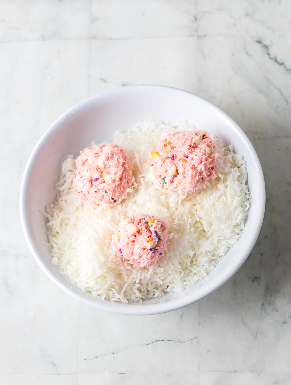 strawberry funfetti balls in a bowl of coconut