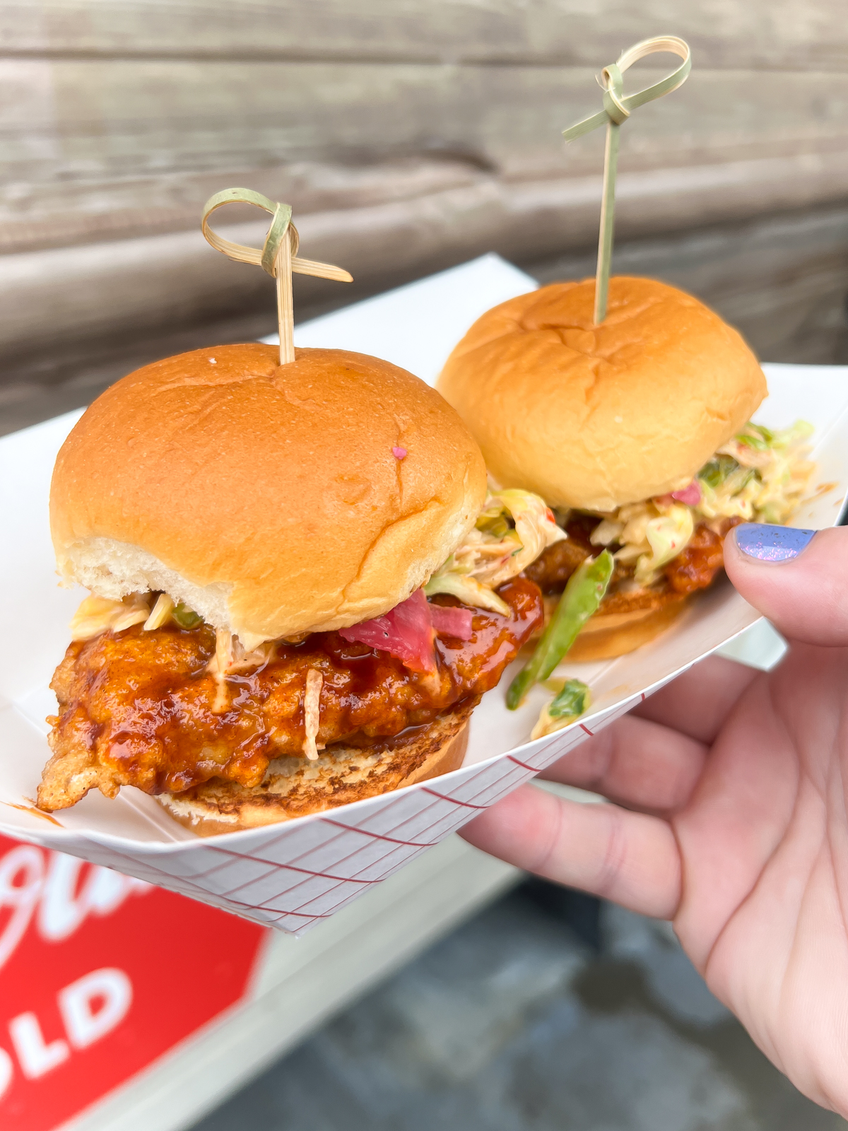 hand holding a tray with two fried chicken sliders