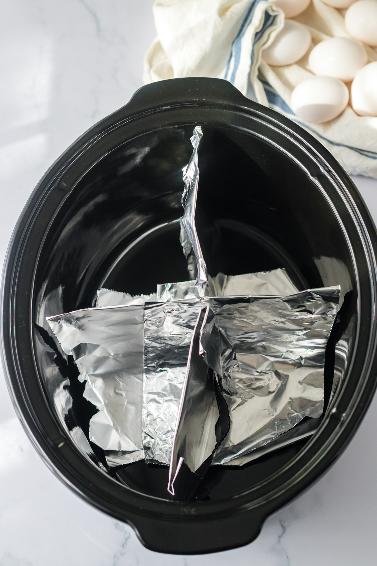 slow cooker with pieces of aluminum foil separating it