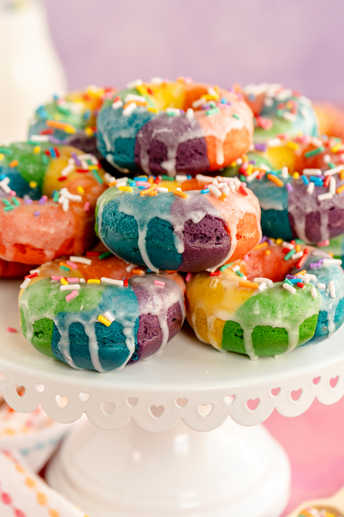 glazed rainbow donuts on a white cake stand