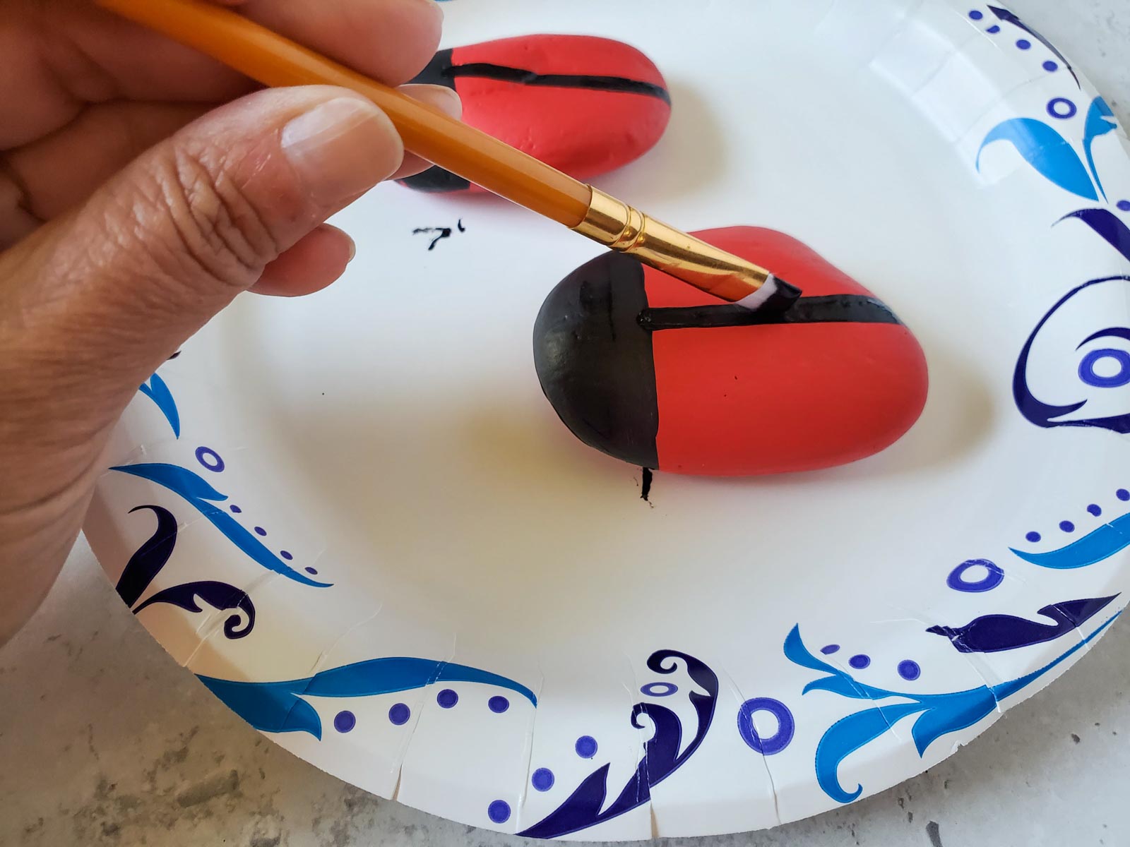 hand painting a line down the back of a ladybug painted rock