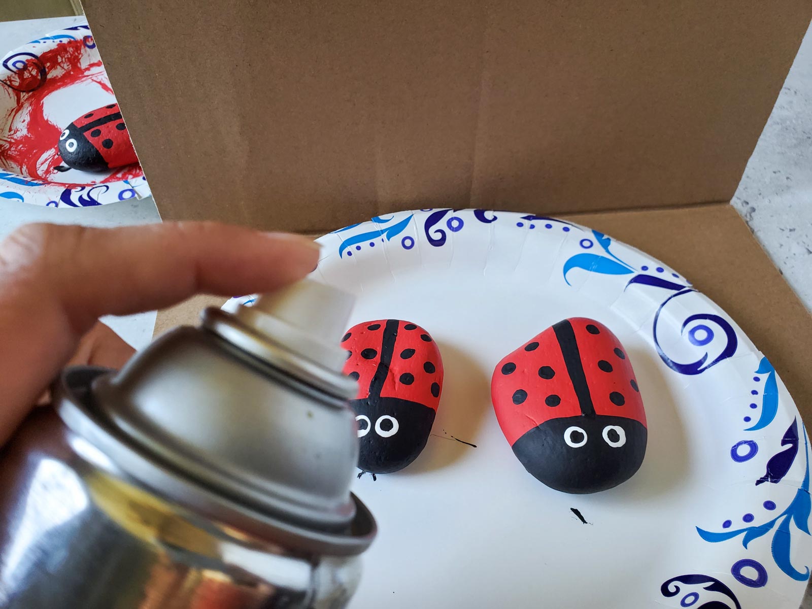 hand spraying clear sealant on ladybug painted rocks