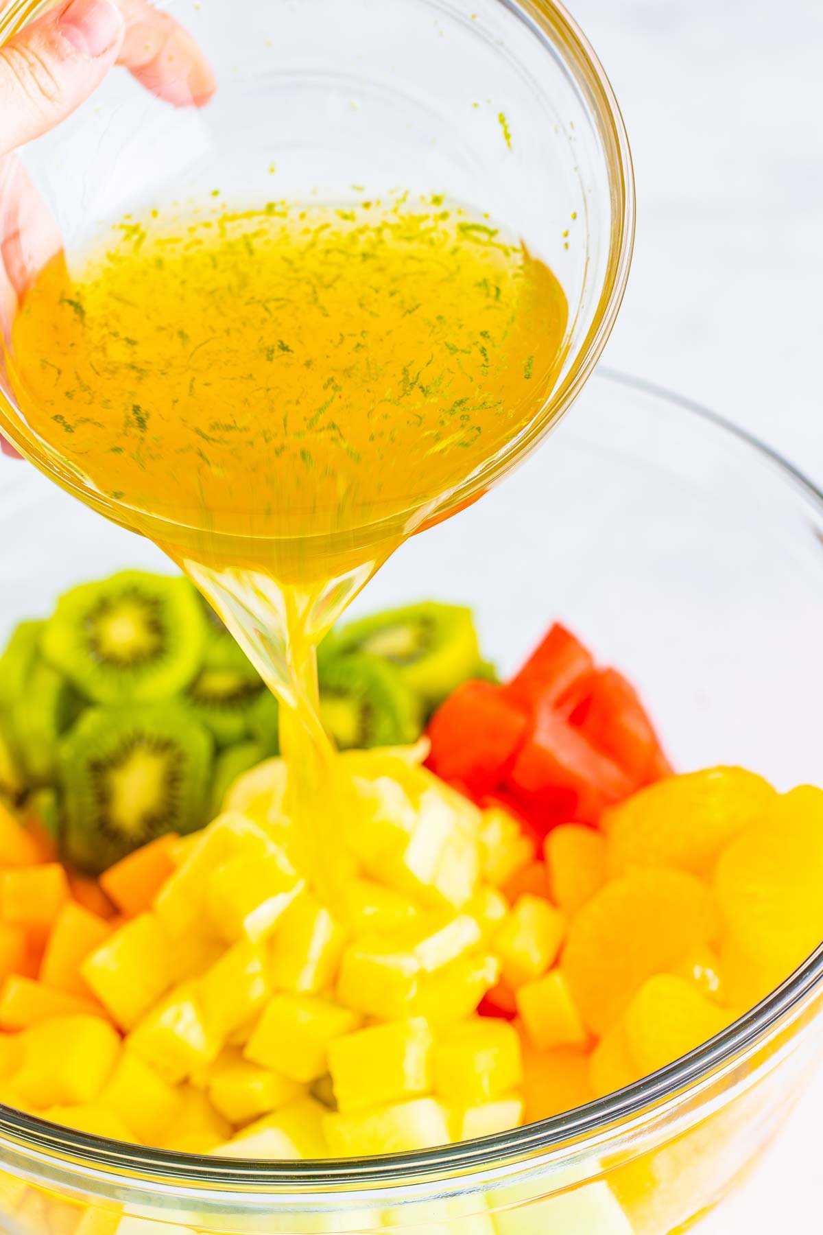 dressing being poured into a bowl of fruit