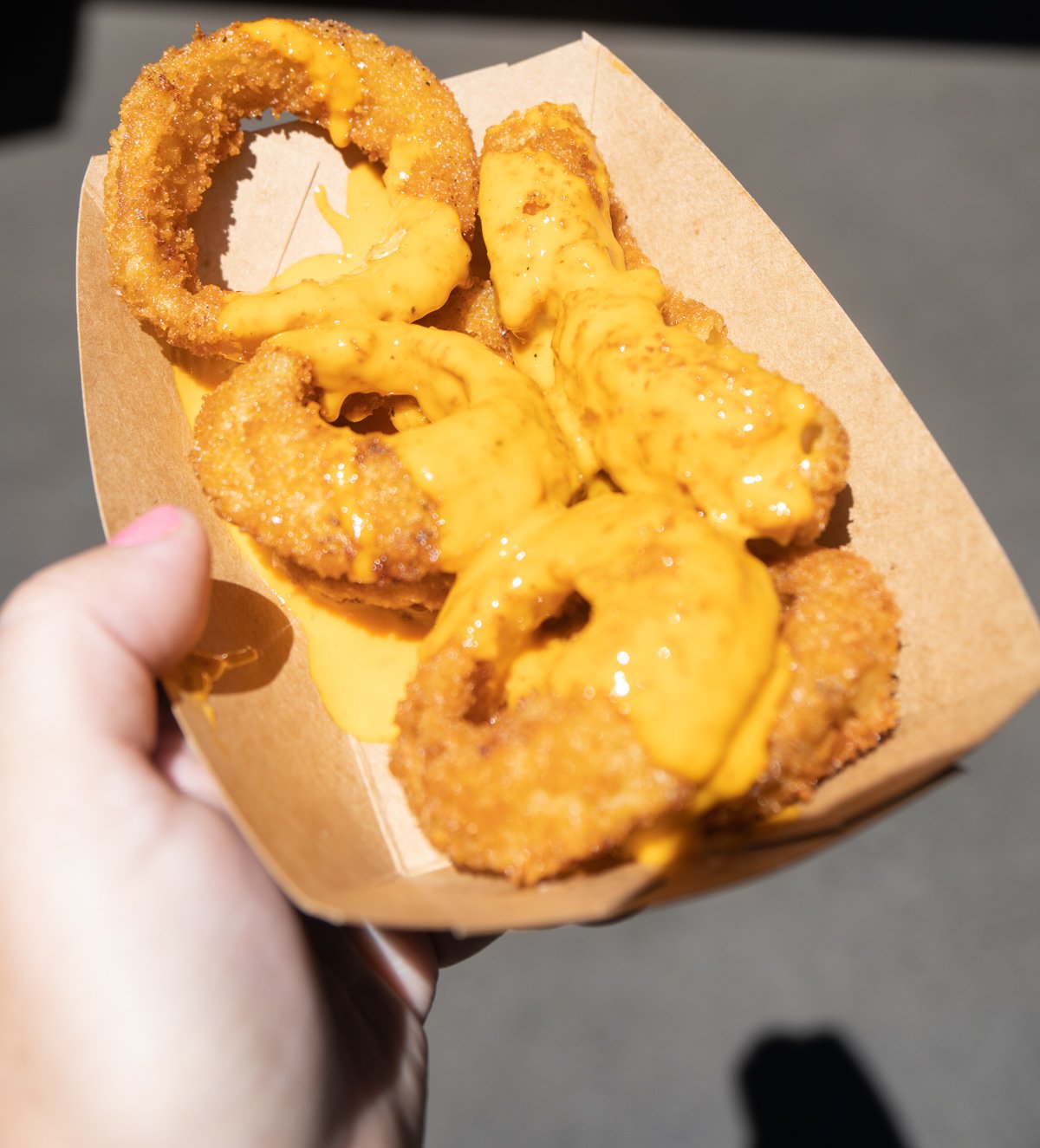hand holding a tray with onion rings topped with cheese sauce