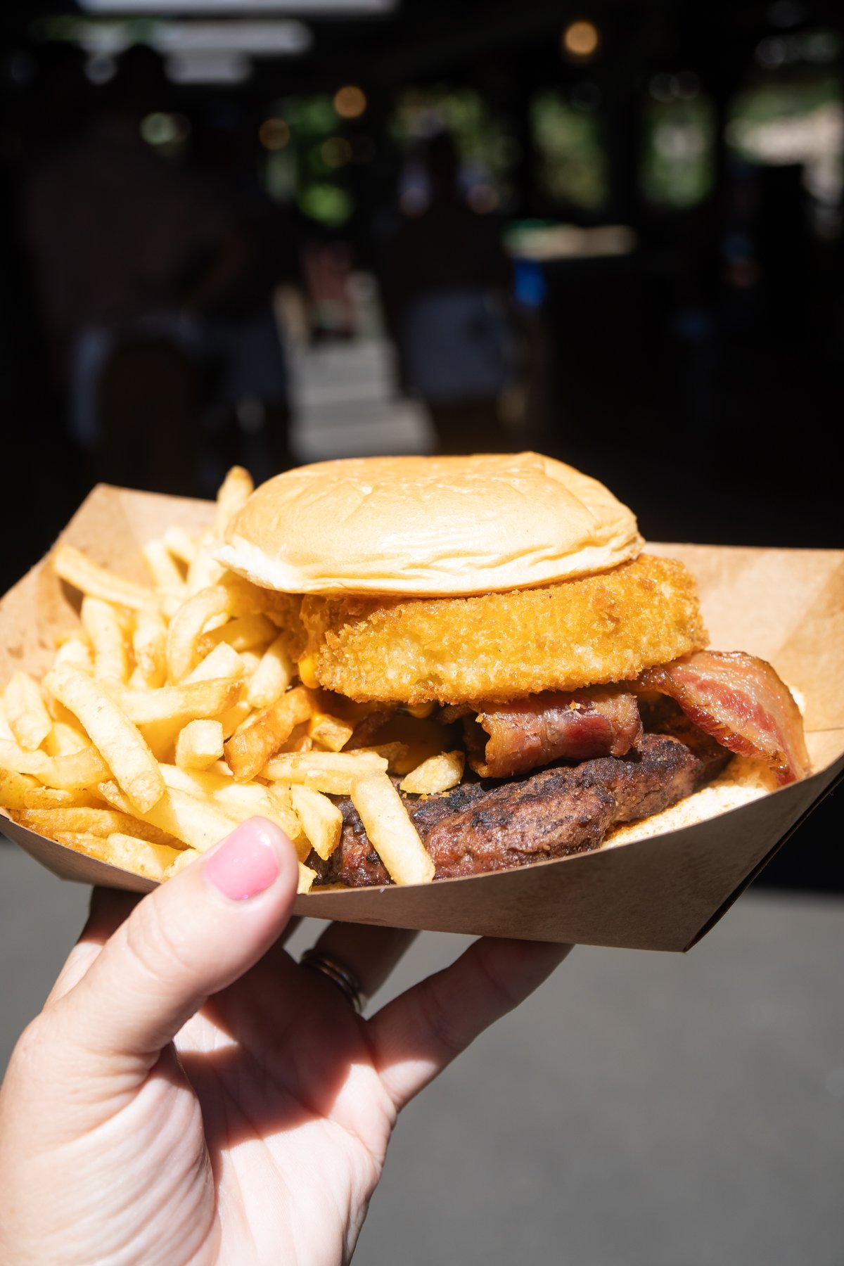 hand holding a tray with a BBQ bacon cheeseburger