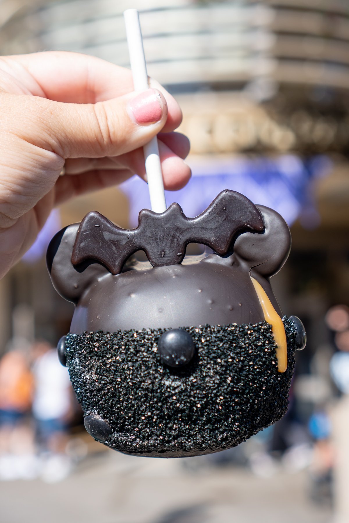 hand holding a dark chocolate caramel apple with a bat