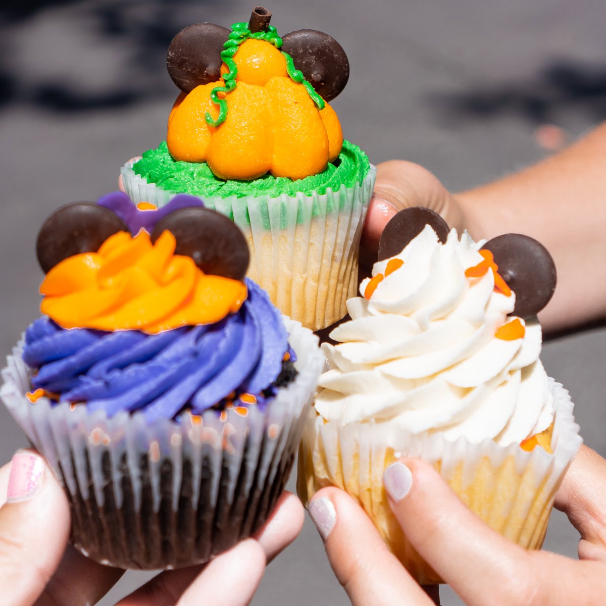 two hands holding three Disney Halloween cupcakes