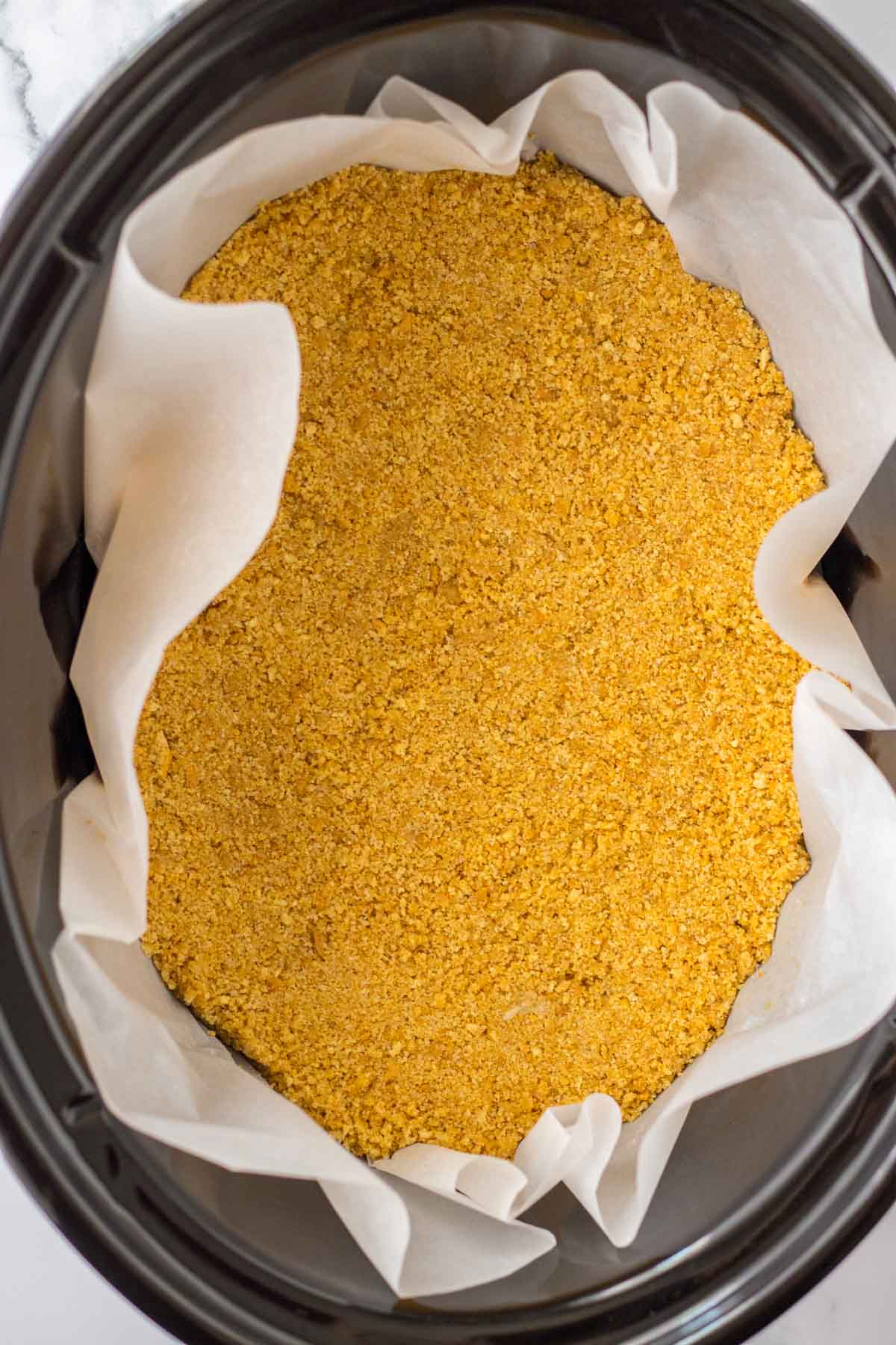 slower cooker lined with parchment paper and graham cracker crumbs