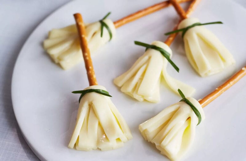 pretzels with cut up string cheese attached at the bottom that look like witch's brooms