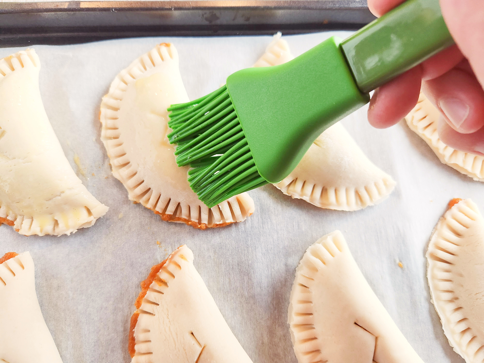 using a silicone brush to add egg wash to unbaked pumpkin pasties