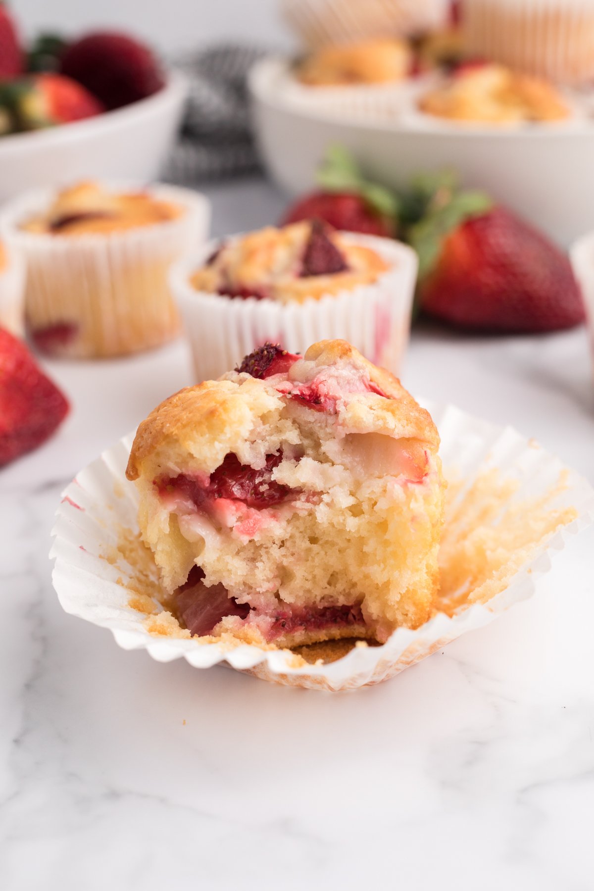 strawberry muffin with a bite taken out of it in a cupcake liner