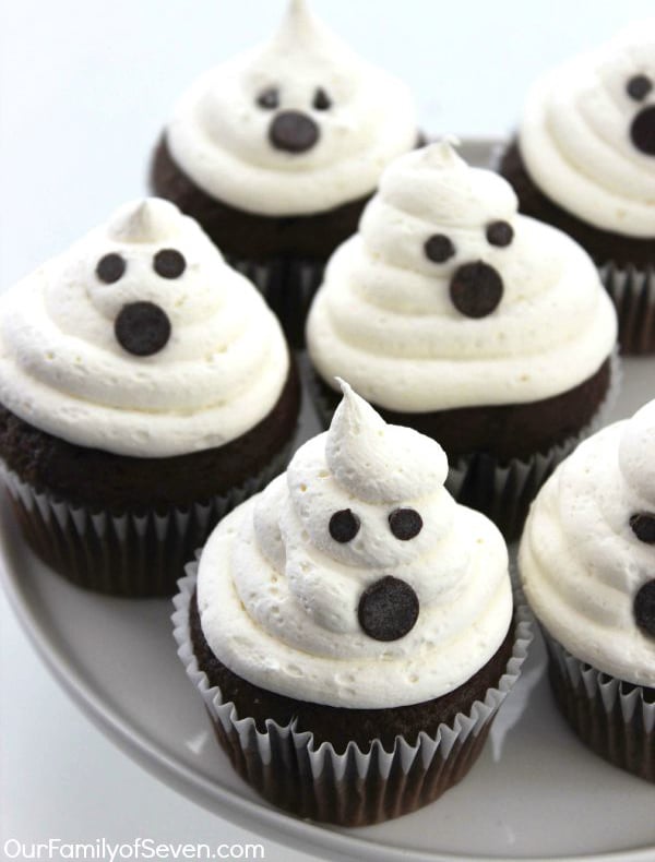 white frosting with ghost faces on top of chocolate cupcakes