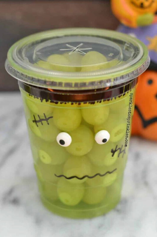 Frankenstein face drawn on plastic cup and filled with green grapes