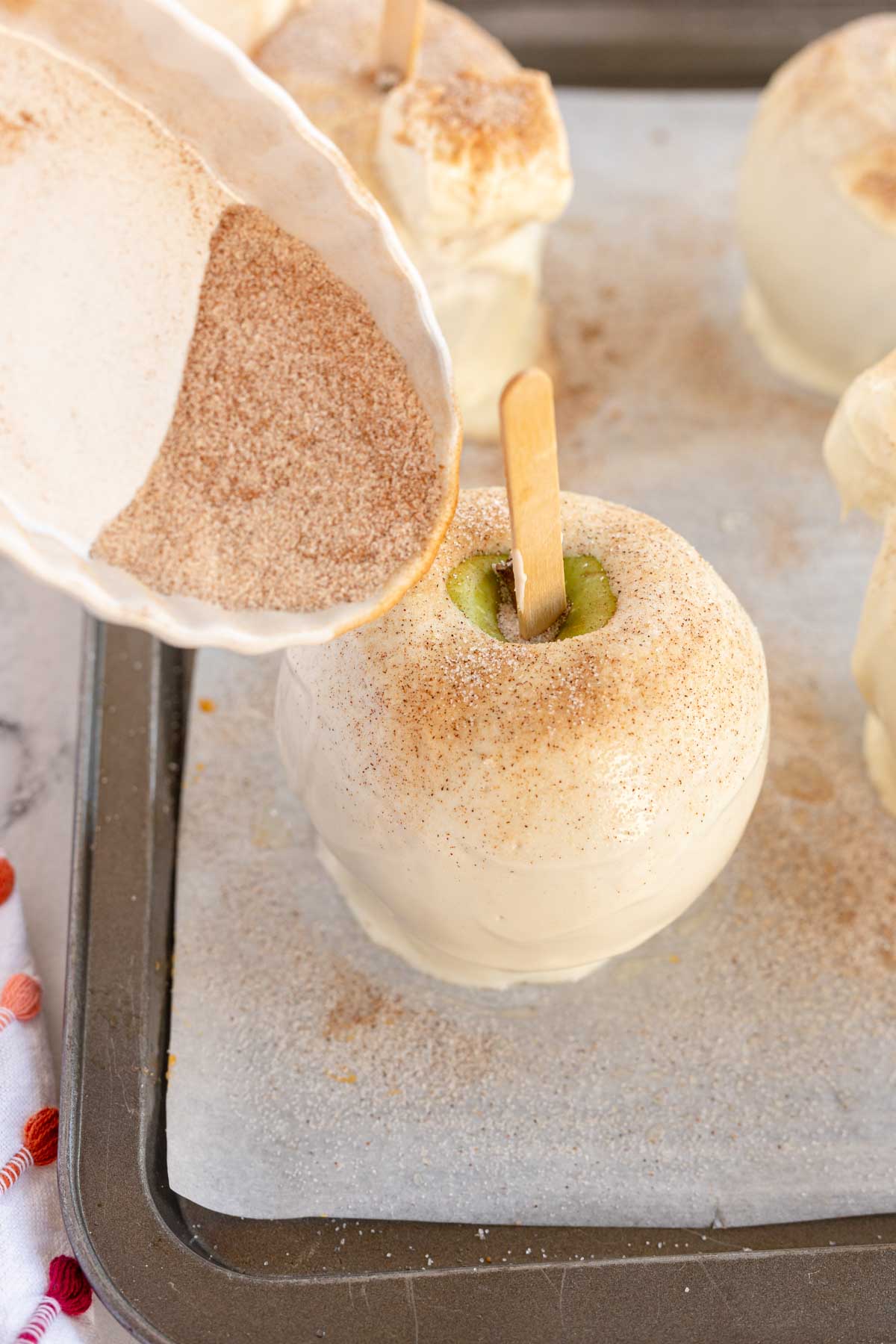 pouring cinnamon sugar onto a white chocolate covered apple