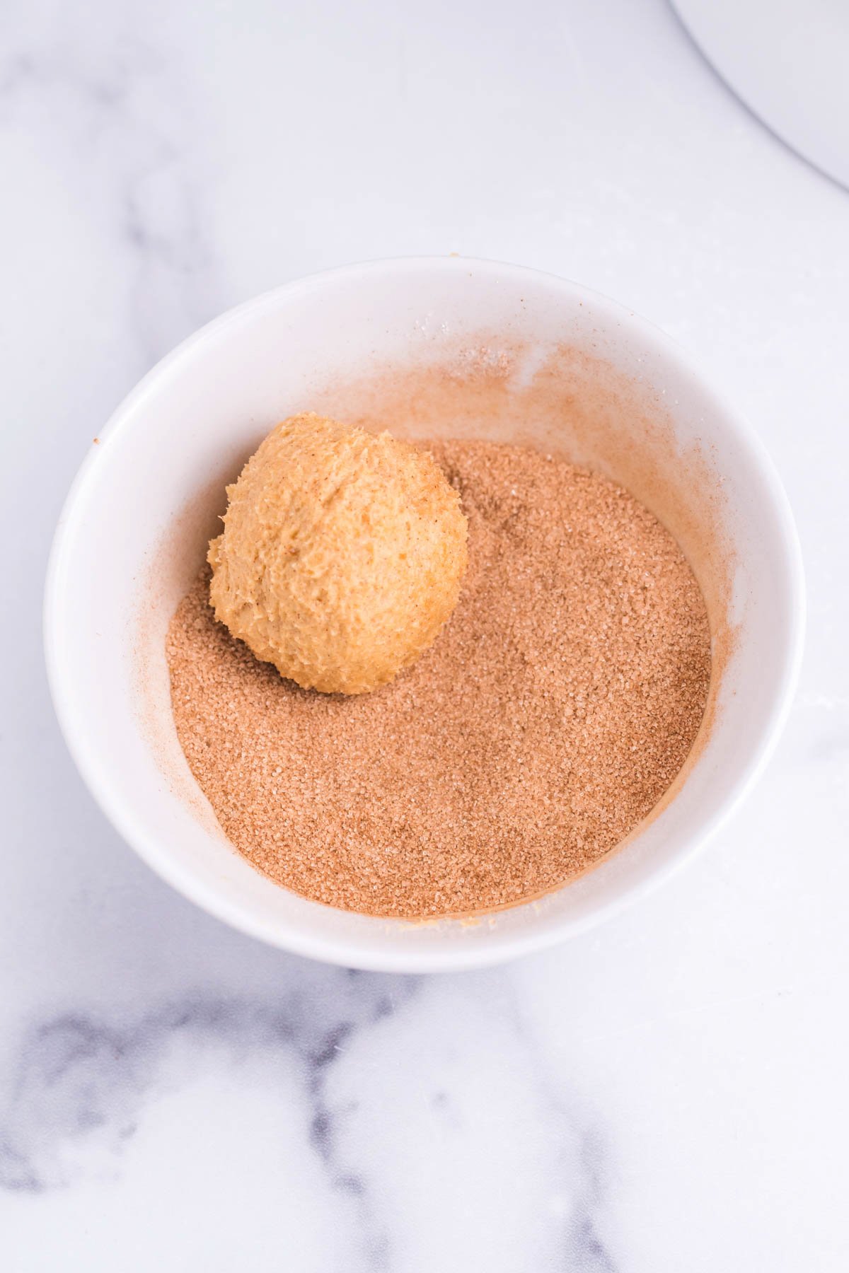 pumpkin snickerdoodle cookie dough ball in a bowl of cinnamon sugar