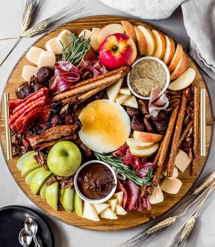 round cheese board with fruits, pretzels, cheese, and meats