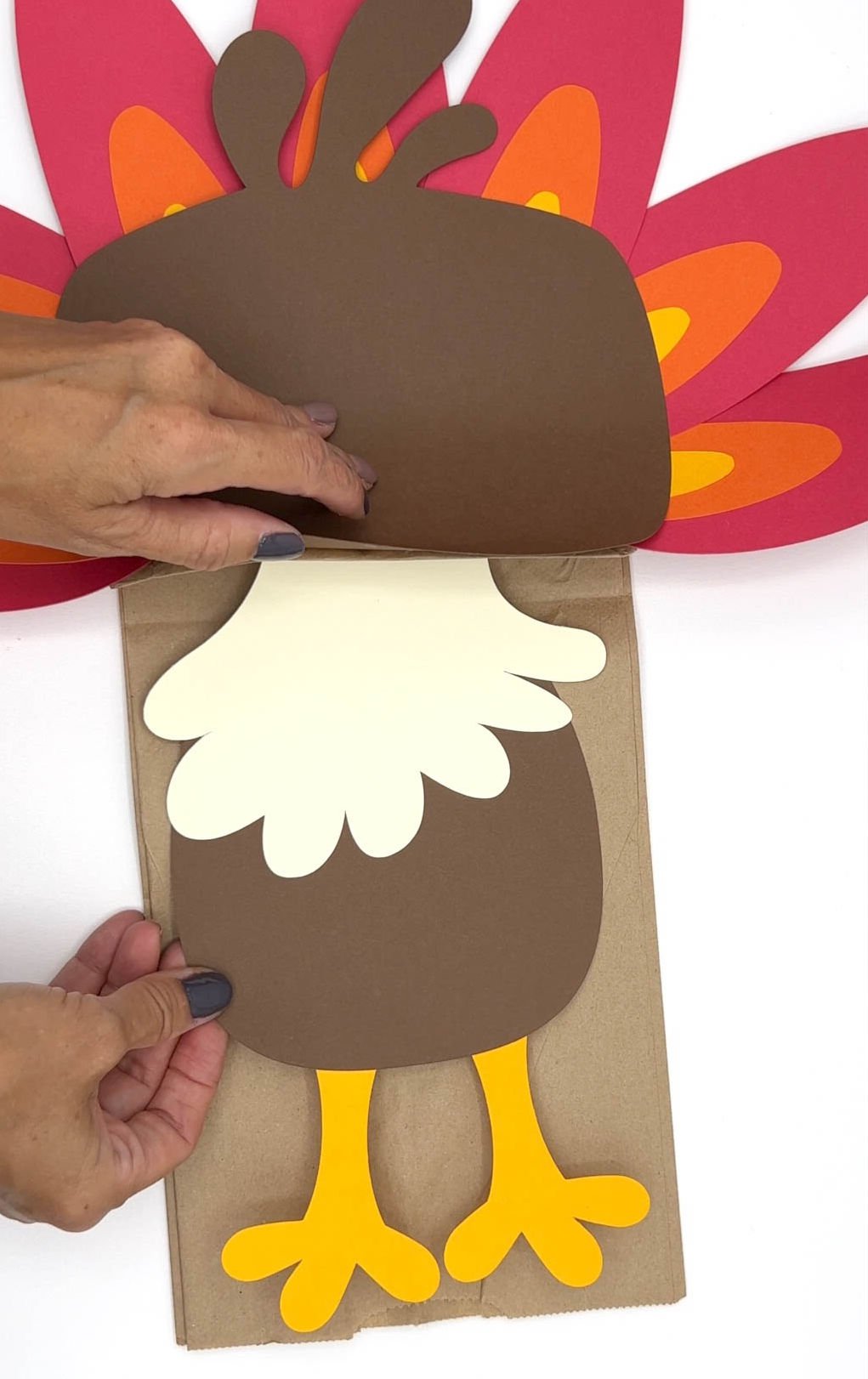 hand adding a piece to a turkey paper bag craft