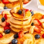 syrup being poured over a plate of mini pancakes