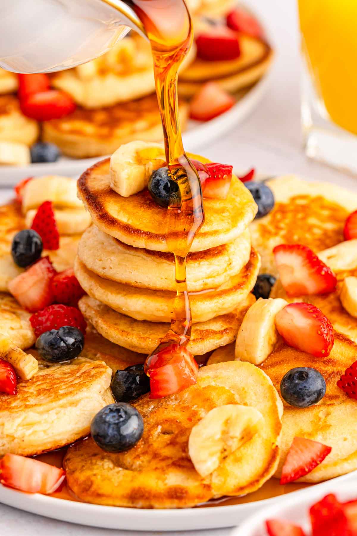 syrup being poured over a plate of mini pancakes