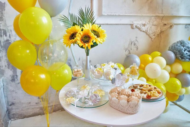 sunflowers in a vase with a variety of yellow sweets on a table