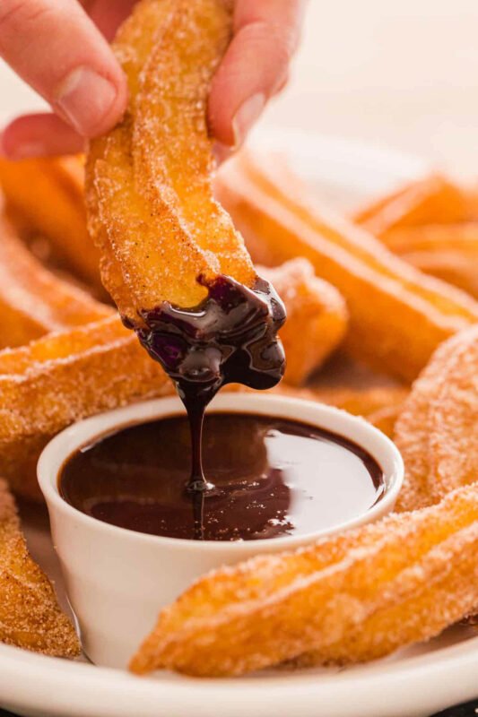 churros being dipped in chocolate sauce