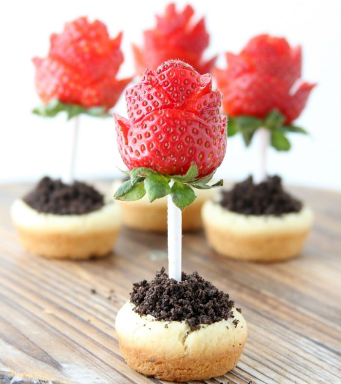 strawberries cut like roses with straw stems into a sugar cookie cup