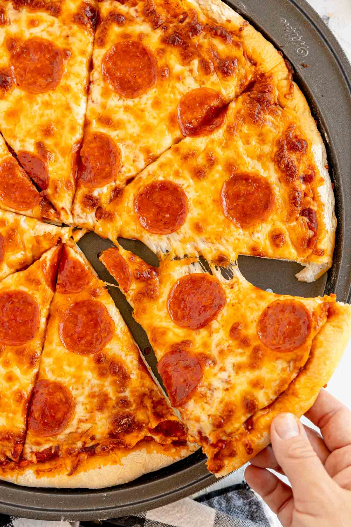 a hand pulling a slice of homemade pepperoni pizza away from a pizza