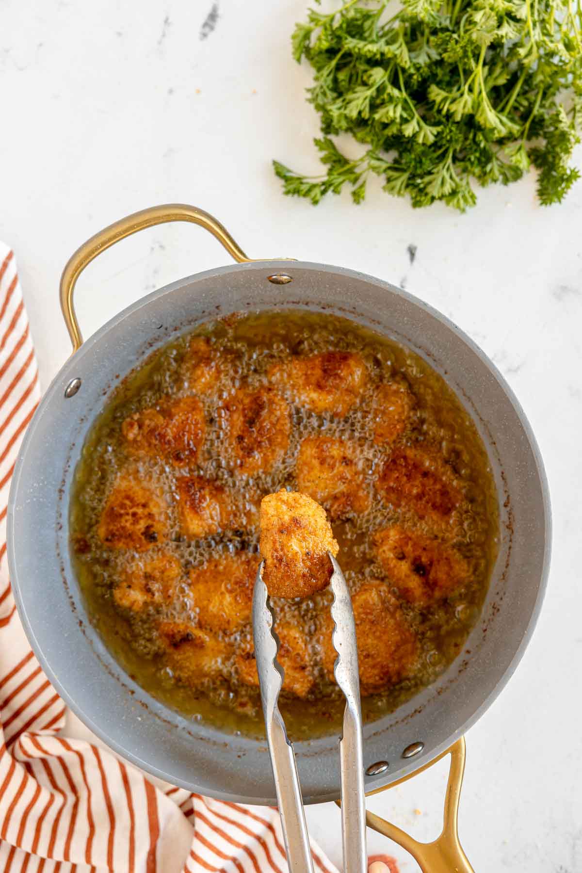 tongs holding a chicken nugget above a pot of hot oil