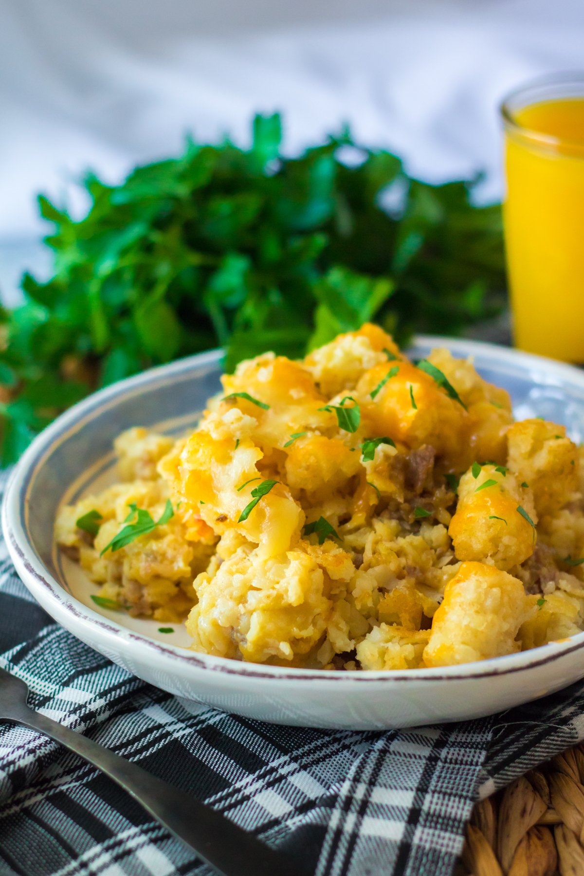 tater tot breakfast casserole on a white plate with some parsley in the background