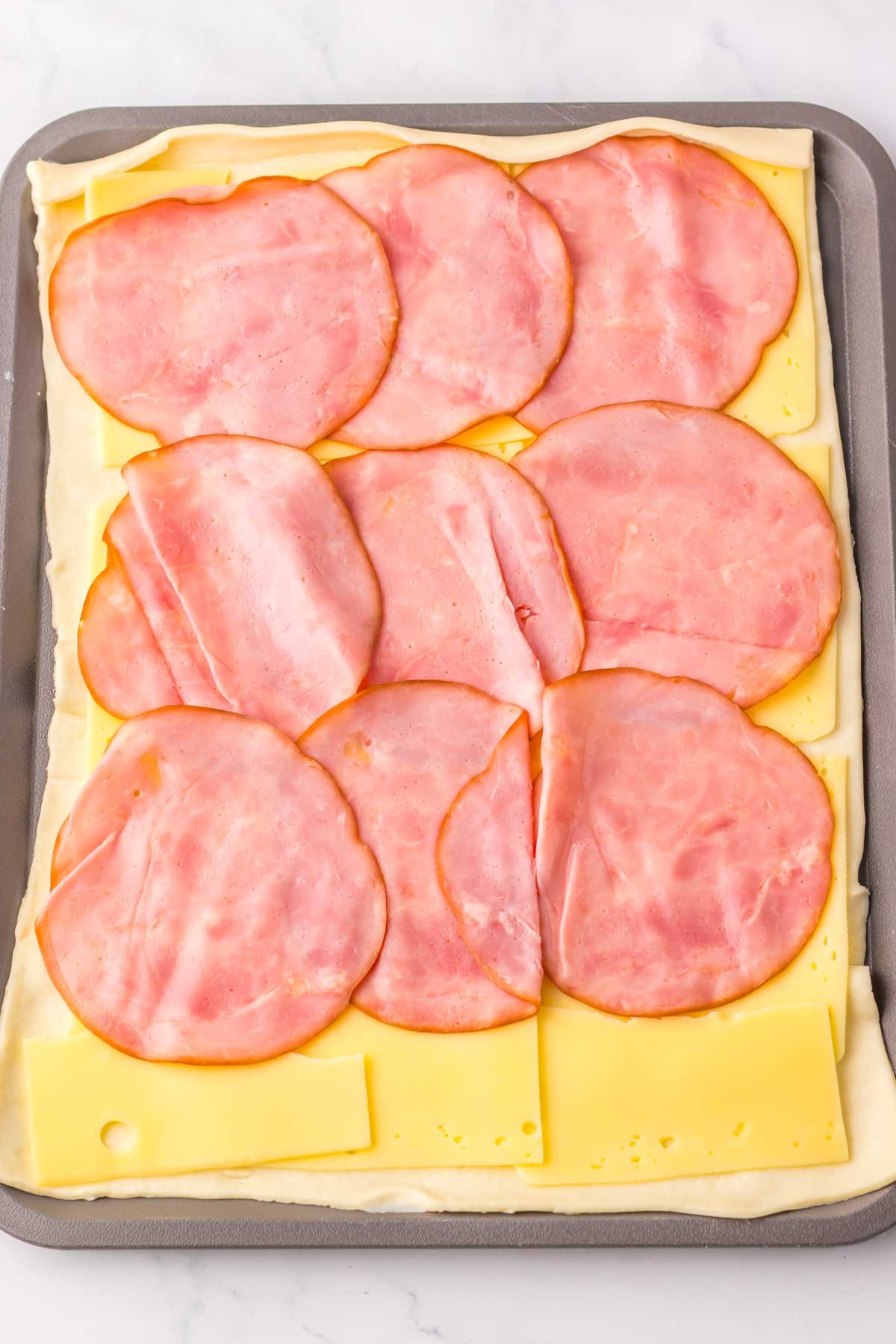 puff pastry topped with ham and cheese on a baking sheet