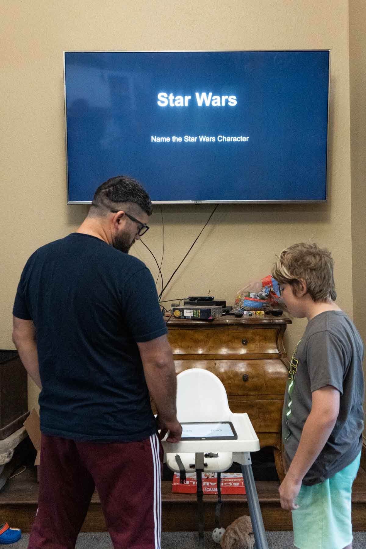 An adult and son standing in front of a TV with Star Wars on it 