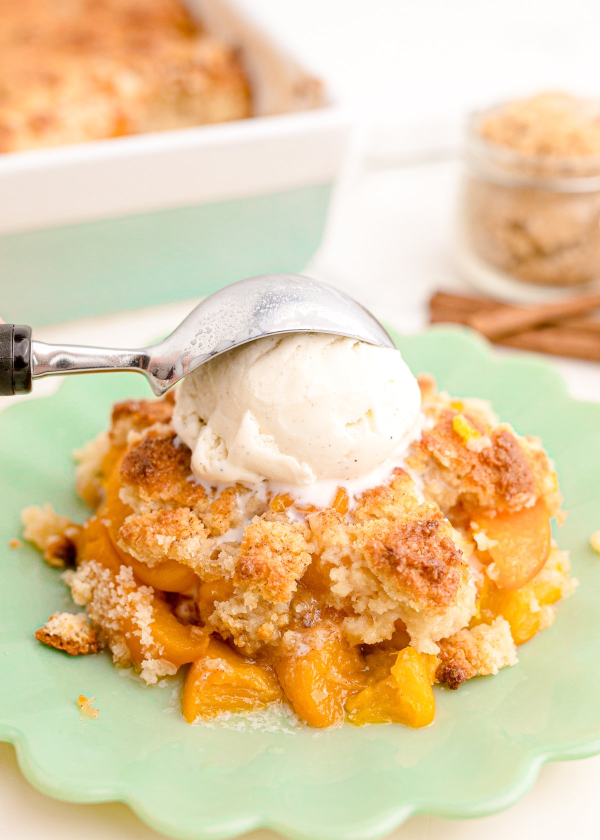ice cream scoop on top of a piece of peach cobbler