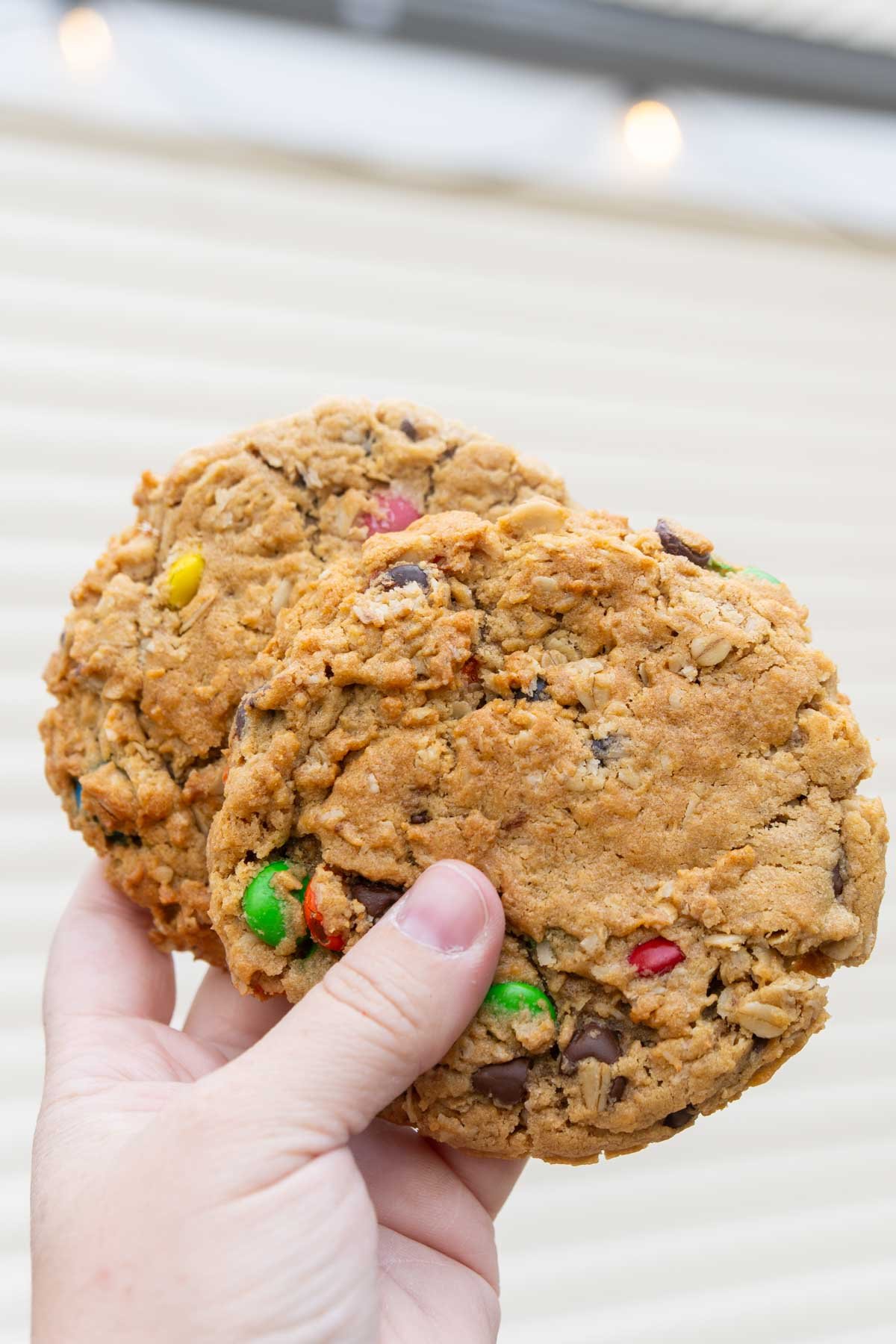 hand holding two monster cookies in front of a garage