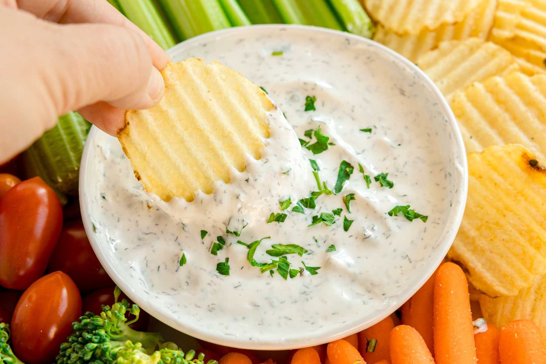 hand dipping a potato chip in veggie dip