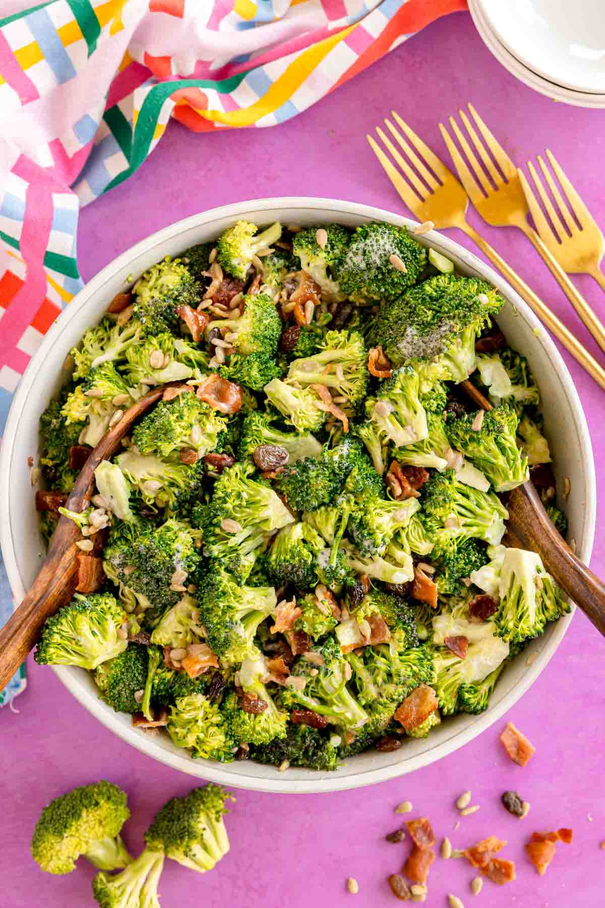 broccoli raisin salad in a white bowl with two wooden spoons