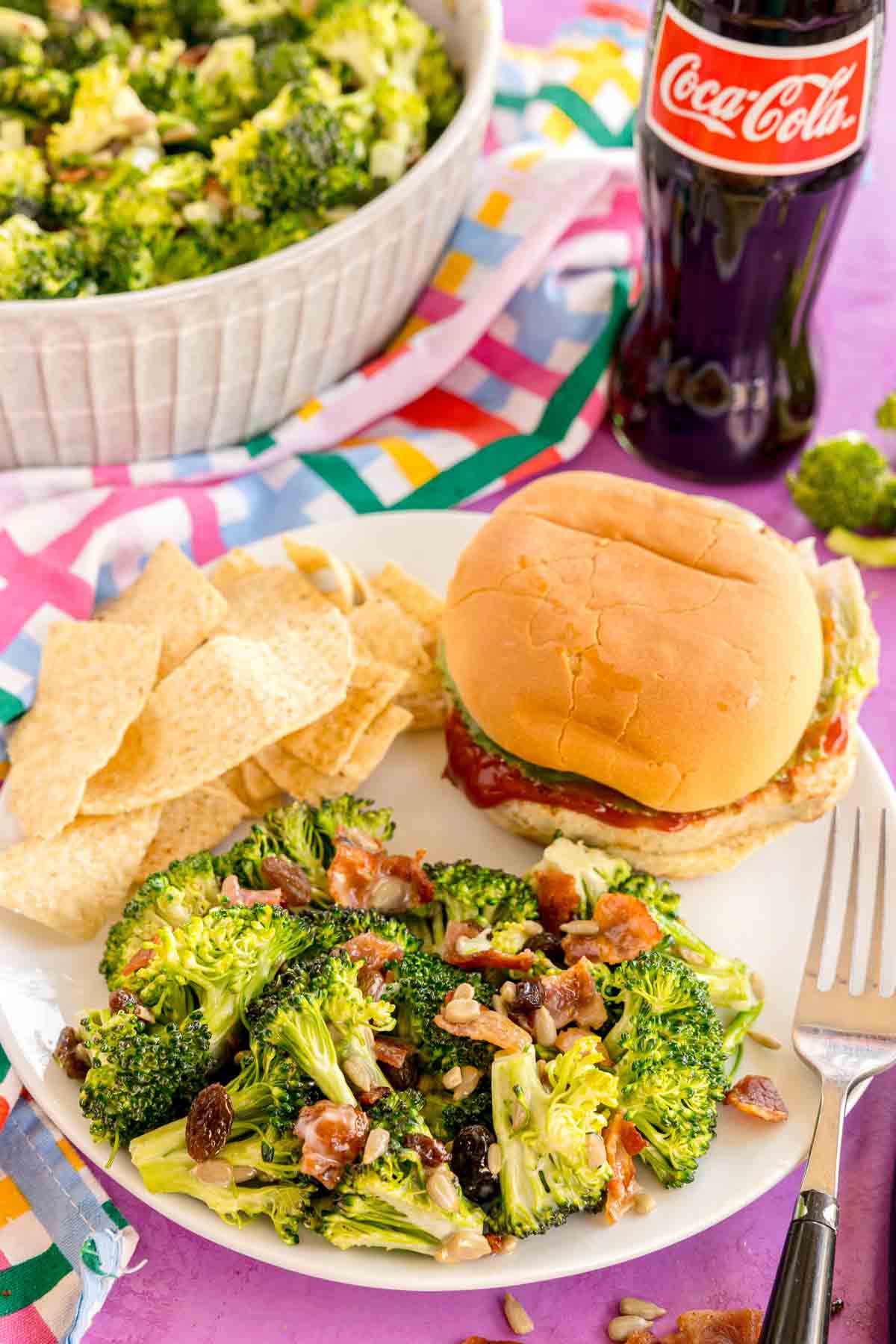 broccoli raisin salad as a side on a white plate with a sandwich and chips