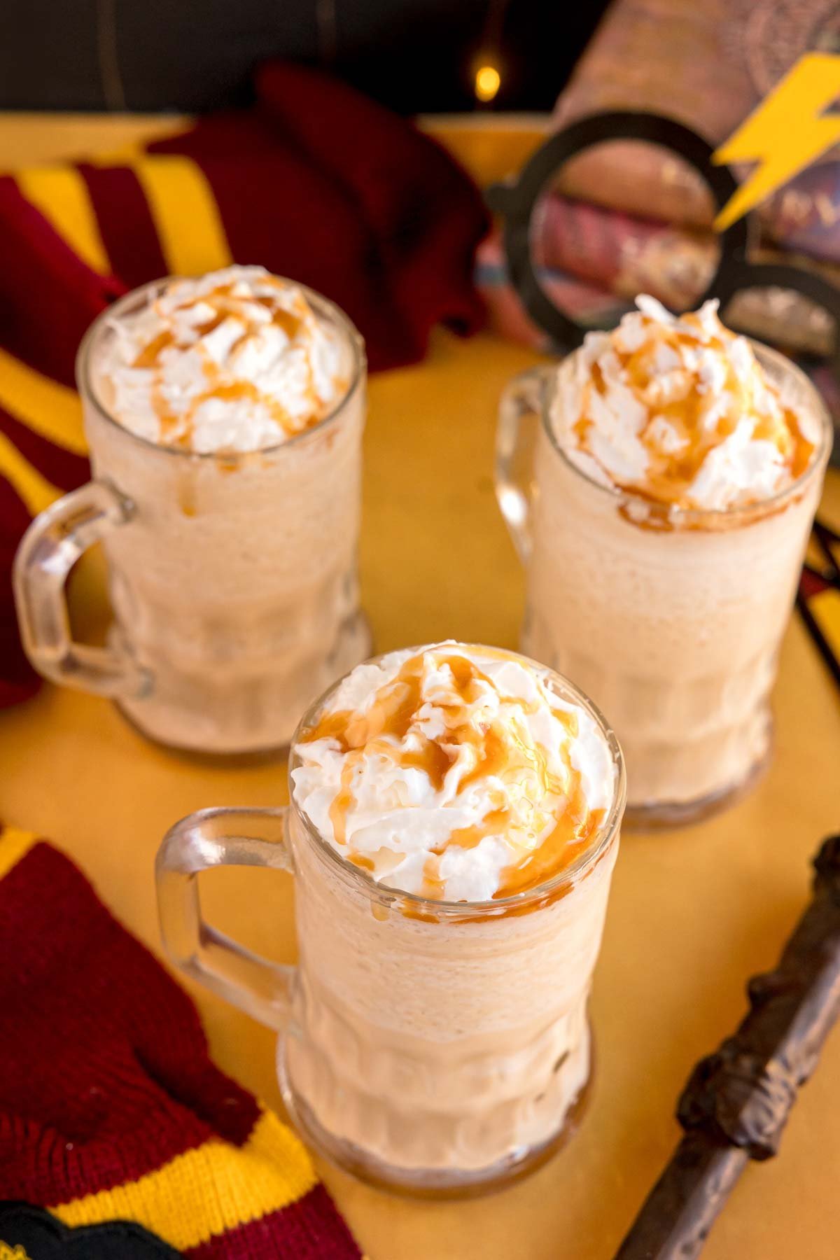 three glass mugs with frozen butterbeer with butterscotch sauce on top