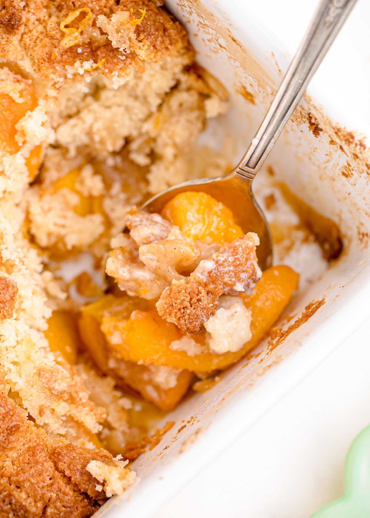 metal spoon in a tray of baked peach cobbler with canned peaches