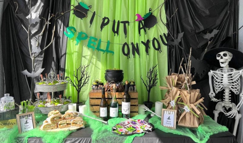 black and green backdrop with witch themed decor and food on a table