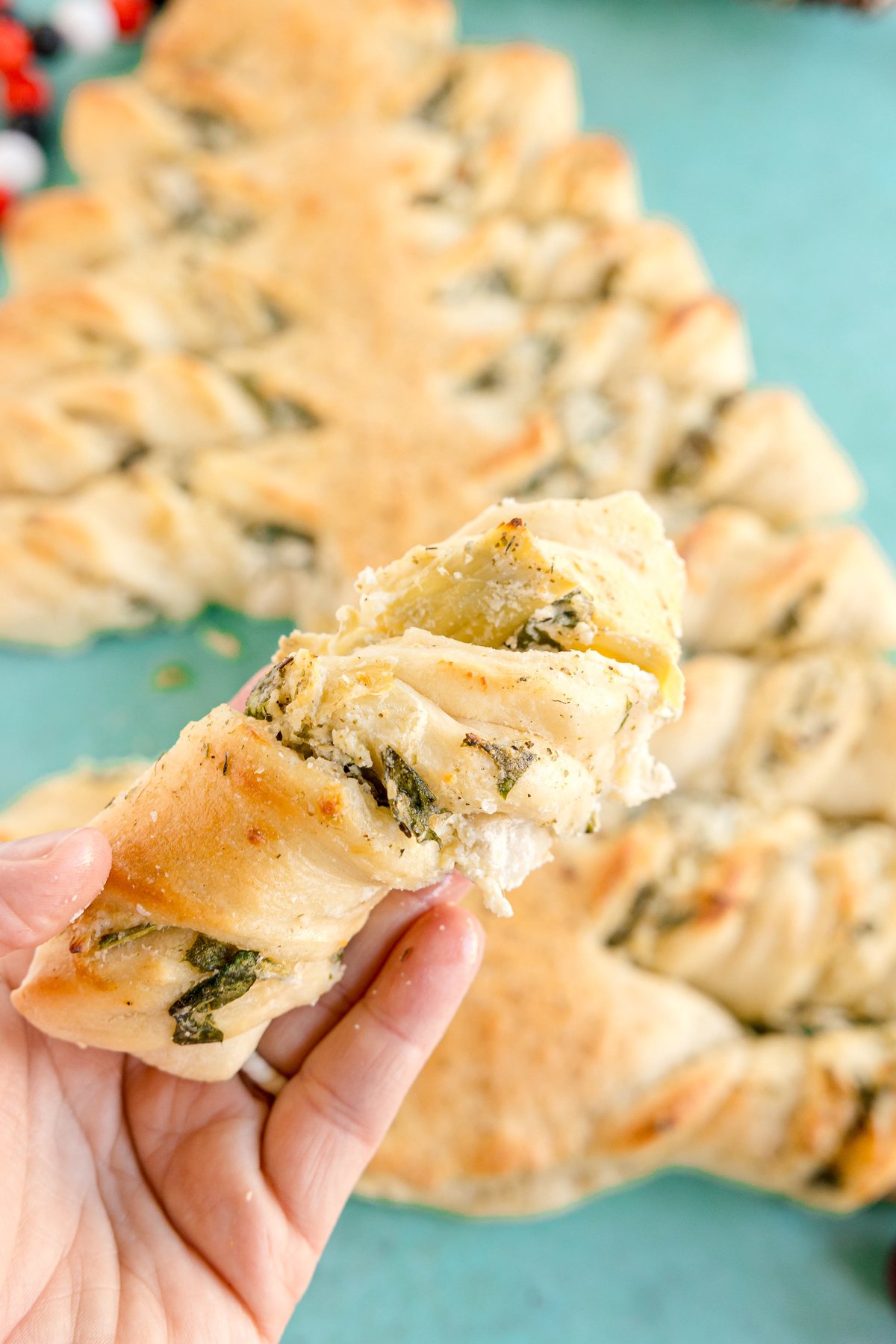 hand holding a piece of a spinach artichoke christmas tree