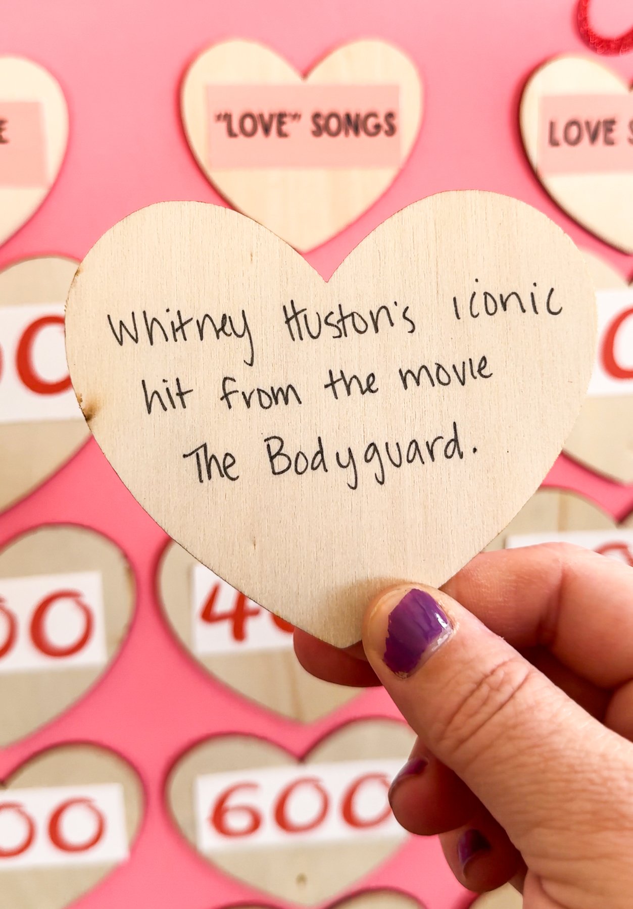 hand holding a wood heart with the question on the back