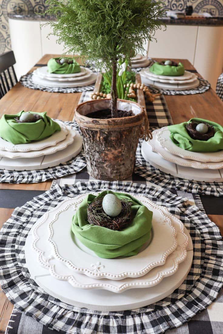 dark neutral colored table with a green napkin wrapped around a small bird nest filled with eggs on a plate stack