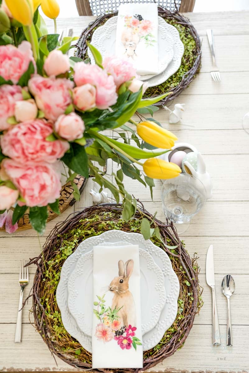 fresh flowers on a table with a wooden placemat, white plates, and bunny napkin