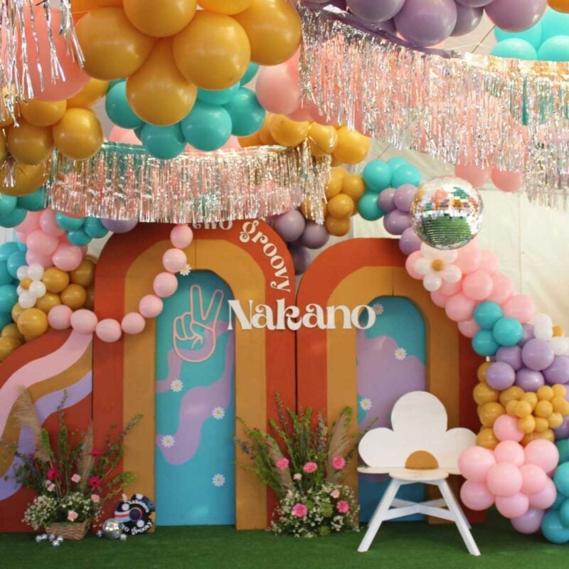 multicolored photo backdrop with balloons, disco balls, and daisies