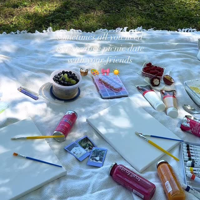 picnic blanket with painting supplies and snacks scattered on it