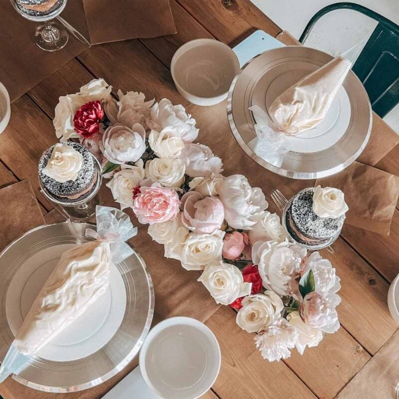 table with flower centerpiece and plates topped with piping bags full of cake frosting