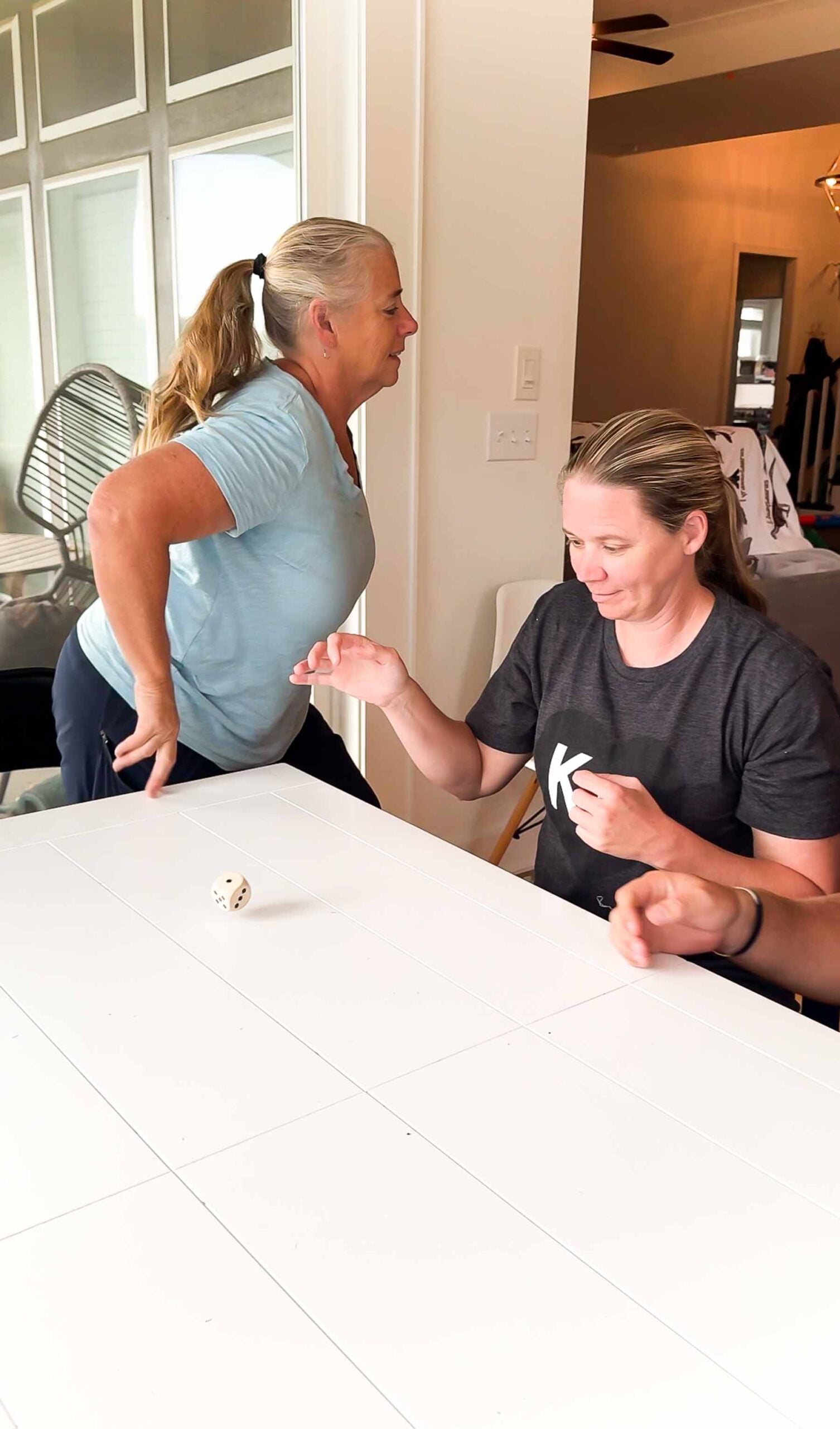 woman standing up and leaving table while other woman is rolling a die